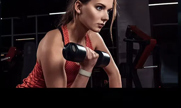 A woman lifts a dumbbell in a gym, the band on her wrist