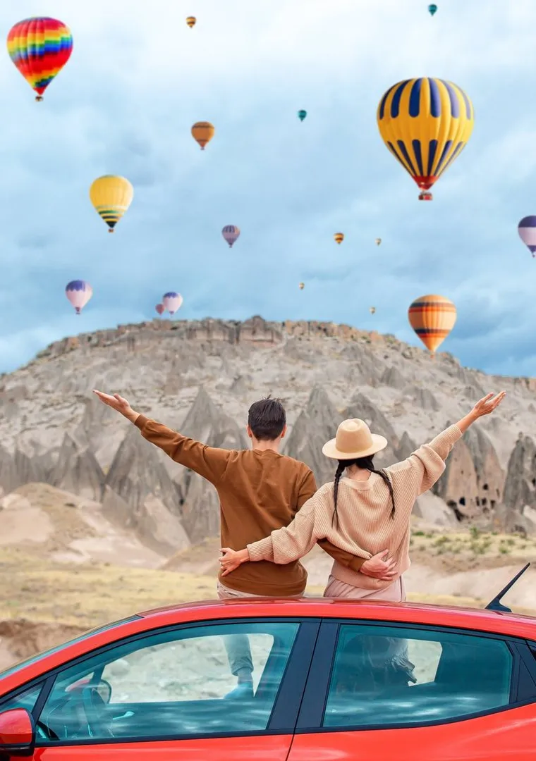 A couple on a car roof watching hot-air balloons over Cappadocia