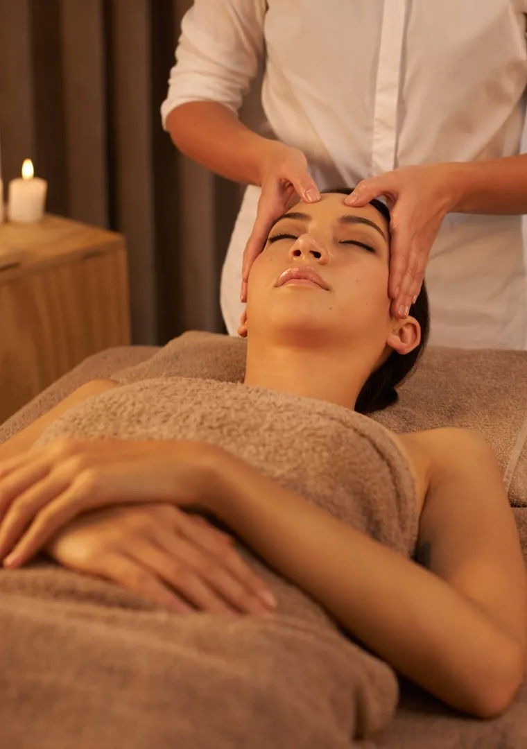 A woman receiving a head massage at a candlelit spa